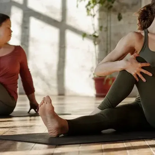 Two women are sitting on yoga mats on the floor.