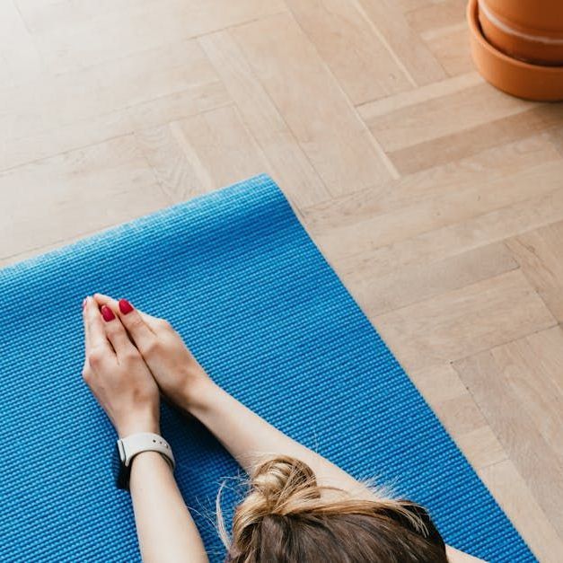 A woman with red nails is laying on a blue yoga mat.