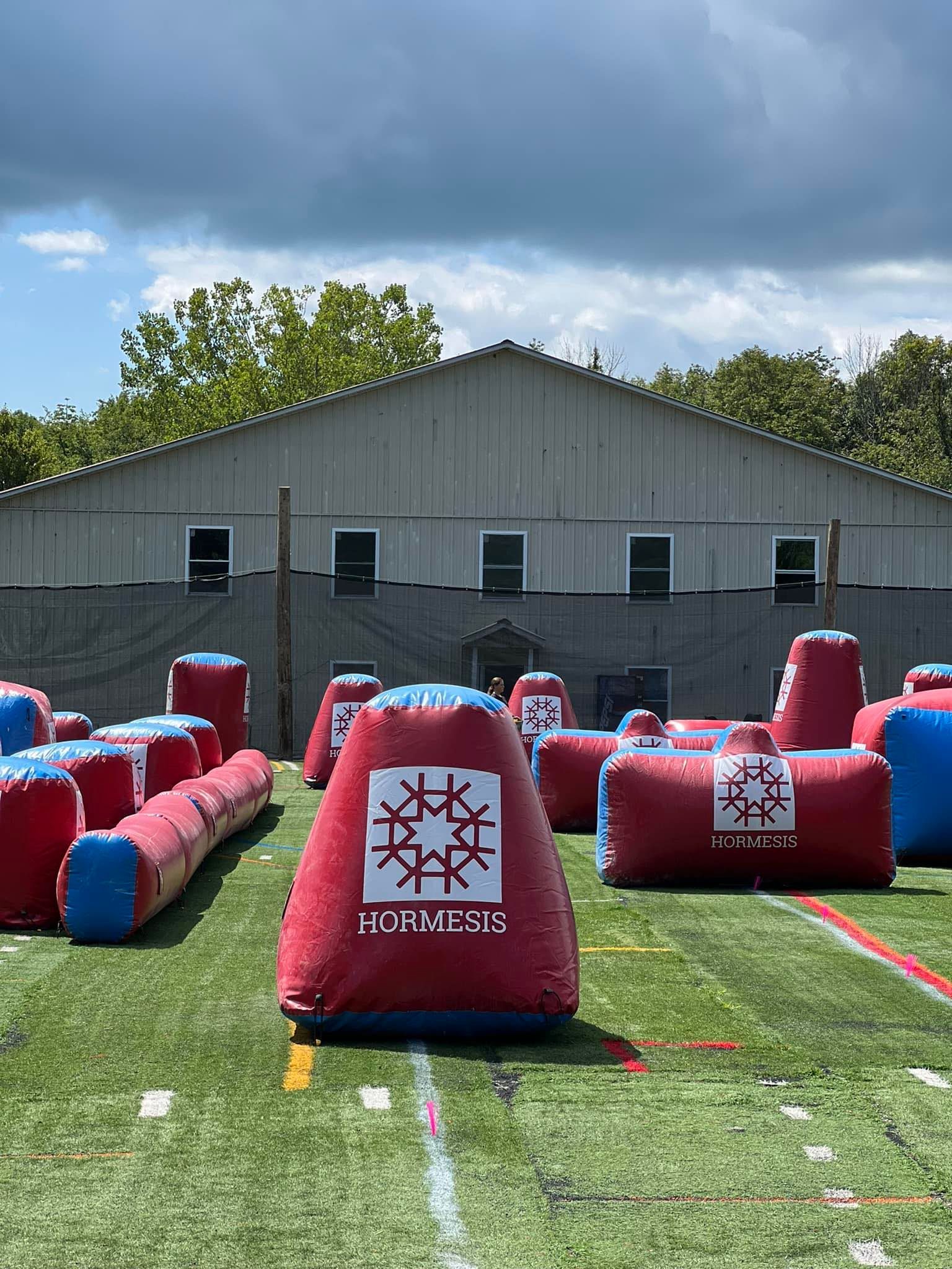 Paintball field with inflatable bunkers; red and blue colors on a green field, building in the background.
