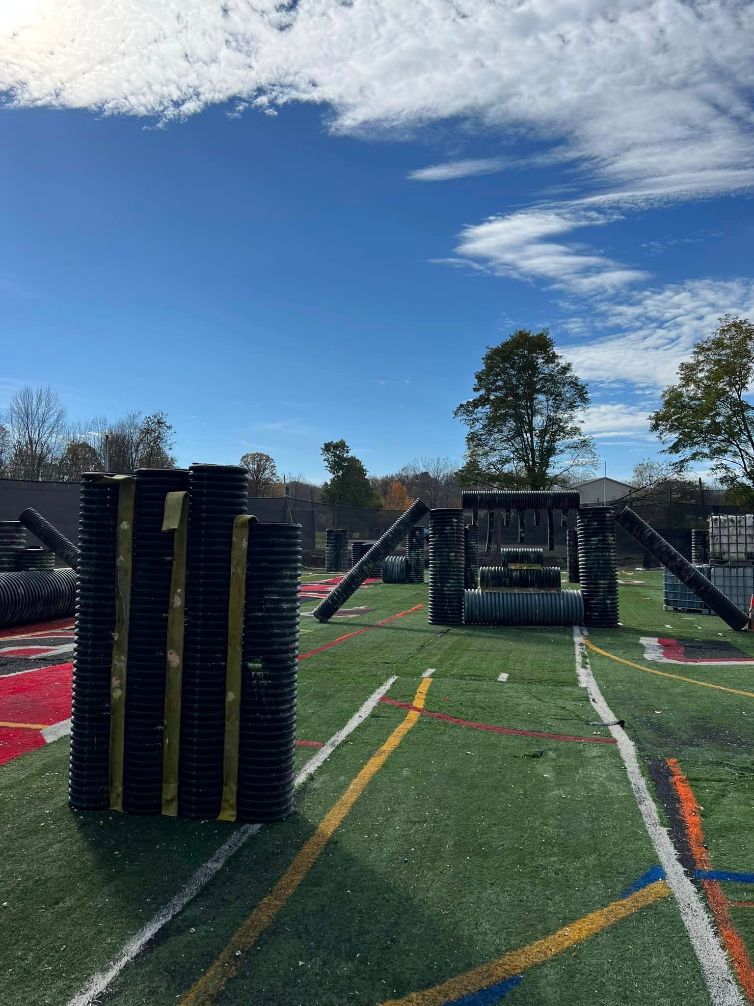 Paintball field with bunkers on a turf field under a blue sky with clouds.