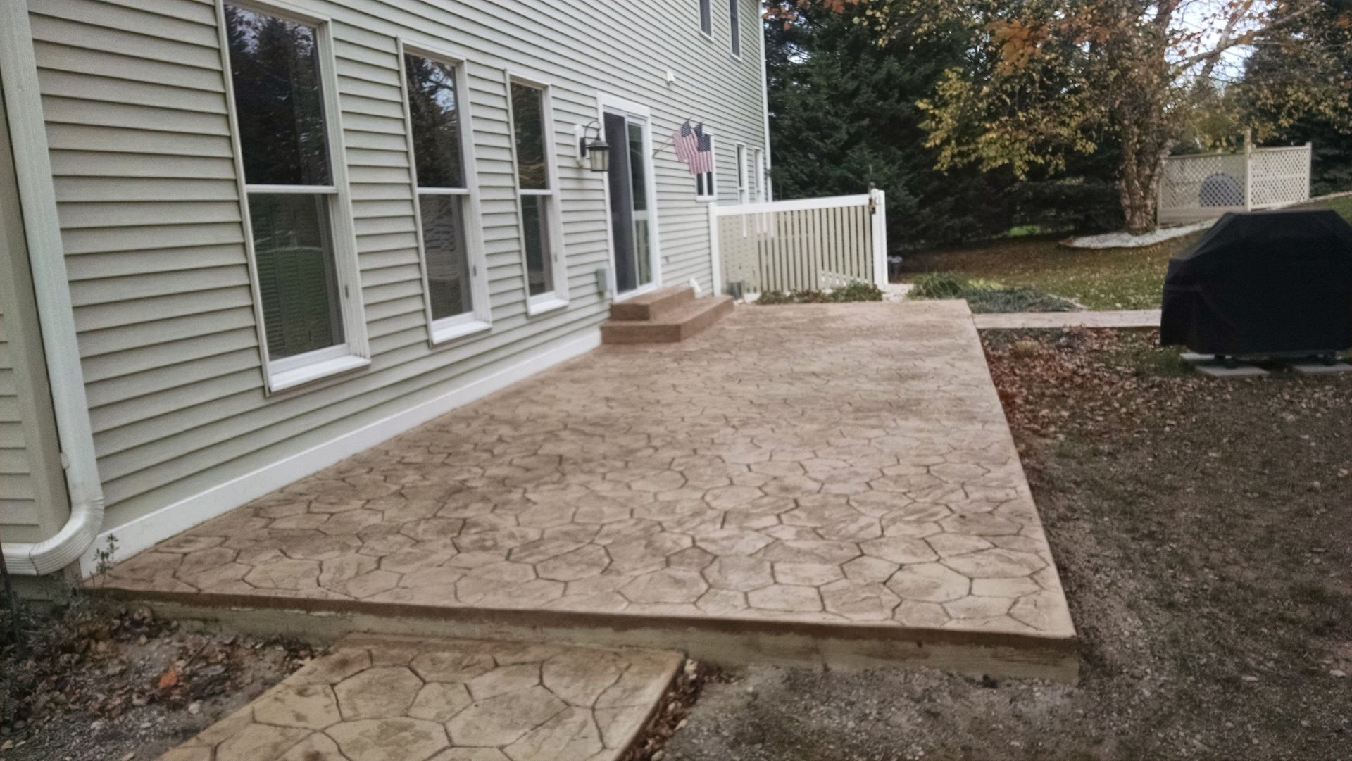 A patio with steps and a grill in front of a house.