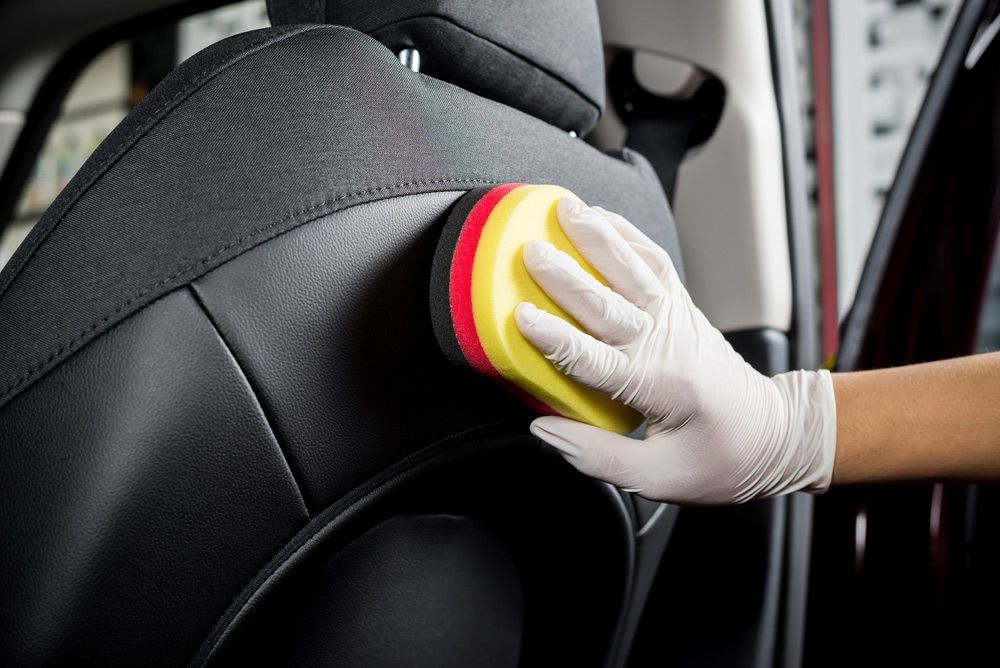 A Person Is Cleaning A Car Seat With A Sponge — Furniture & Auto Pride in South West Rocks, NSW