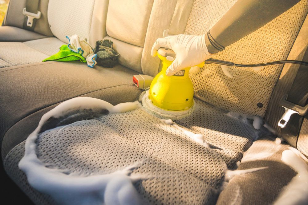 A Person Is Cleaning The Back Seat Of A Car With A Vacuum Cleaner — Furniture & Auto Pride in Harrington, NSW