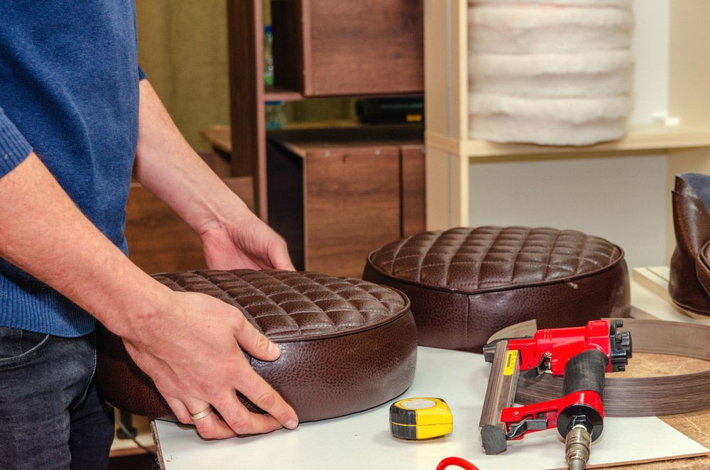 A Man Is Fixing A Brown Leather Ottoman With A Stapler — Furniture & Auto Pride in Lake Cathie, NSW