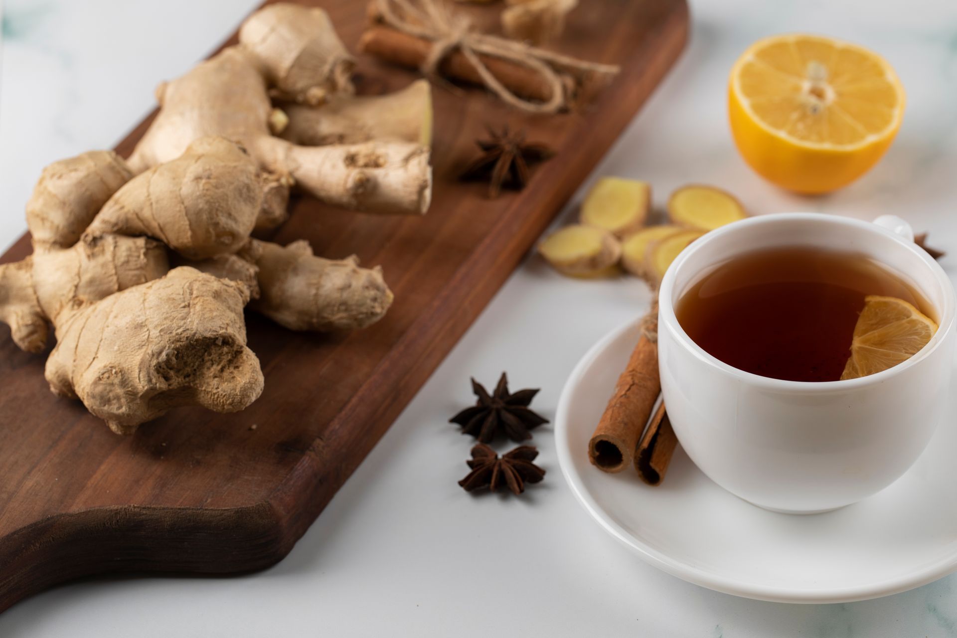 Gingembre, bâtons de cannelle, anis étoilé et une tasse de thé sur une planche à découper en bois.