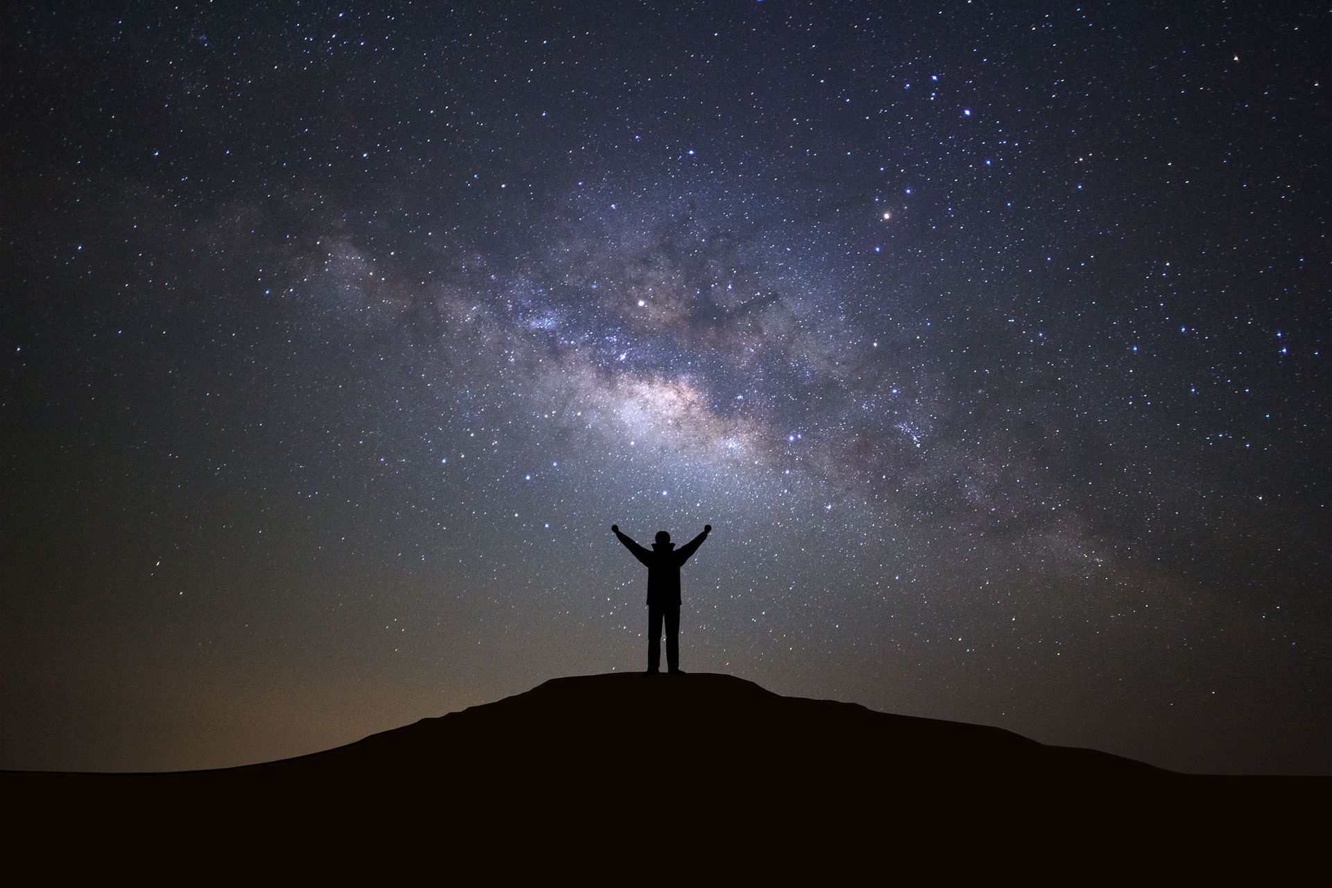 Silhouetted person on a hill with arms raised under a starry Milky Way sky