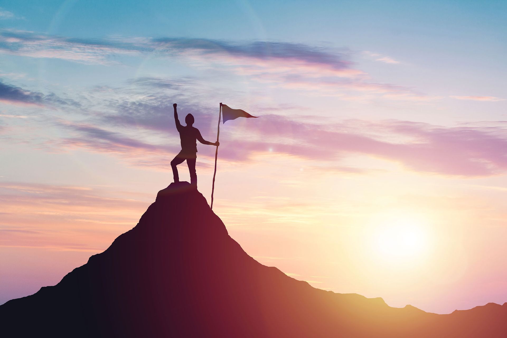 Silhouette of person on mountain peak with flag, celebrating sunset.