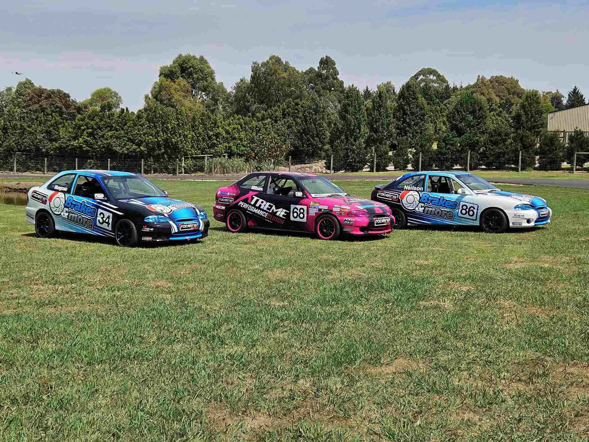 A group of race cars are parked in a grassy field.