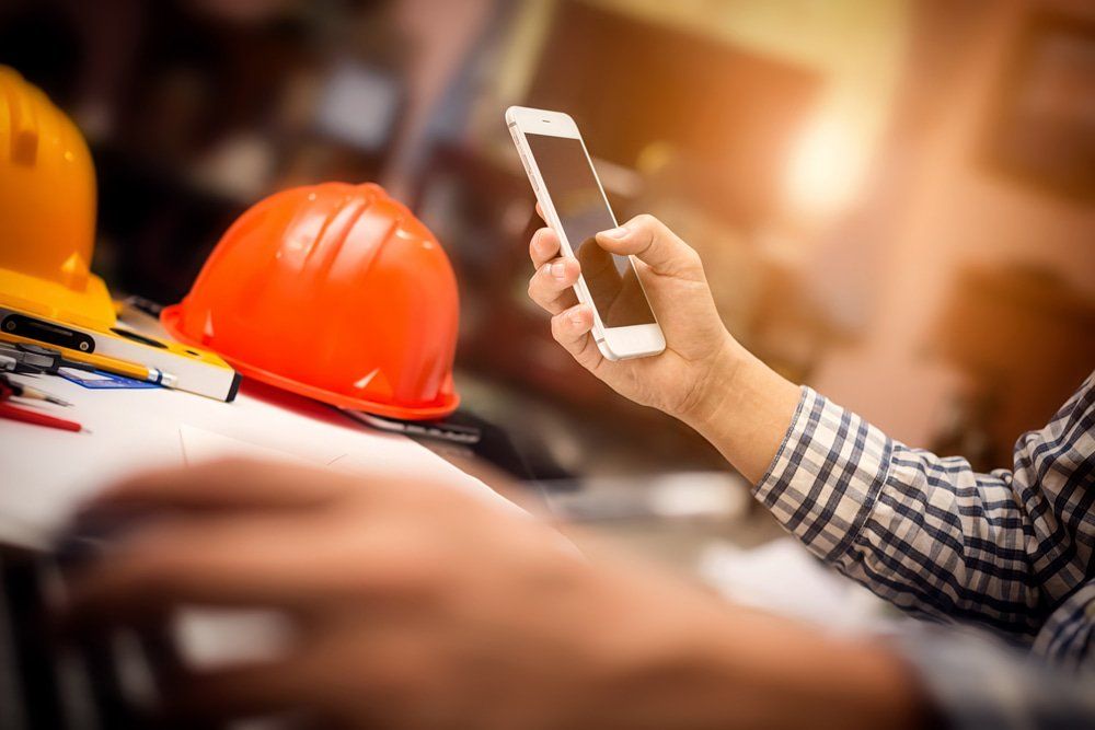 Man Holding A Smartphone At Construction Office Desk — Cemak Constructions in Port Macquarie, NSW