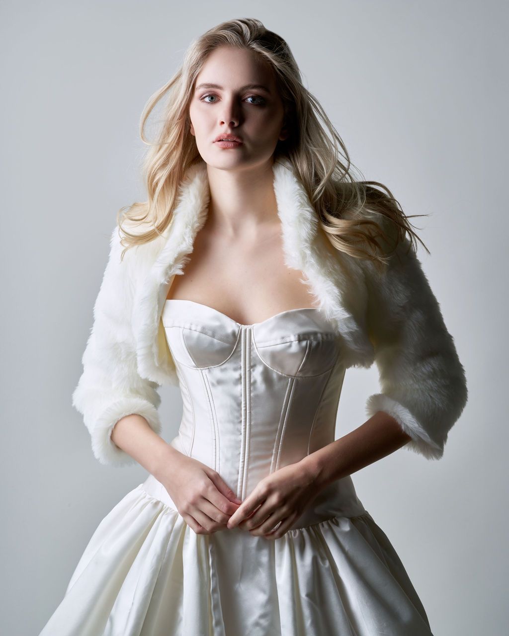 A woman in a white dress is wearing a white fur jacket.