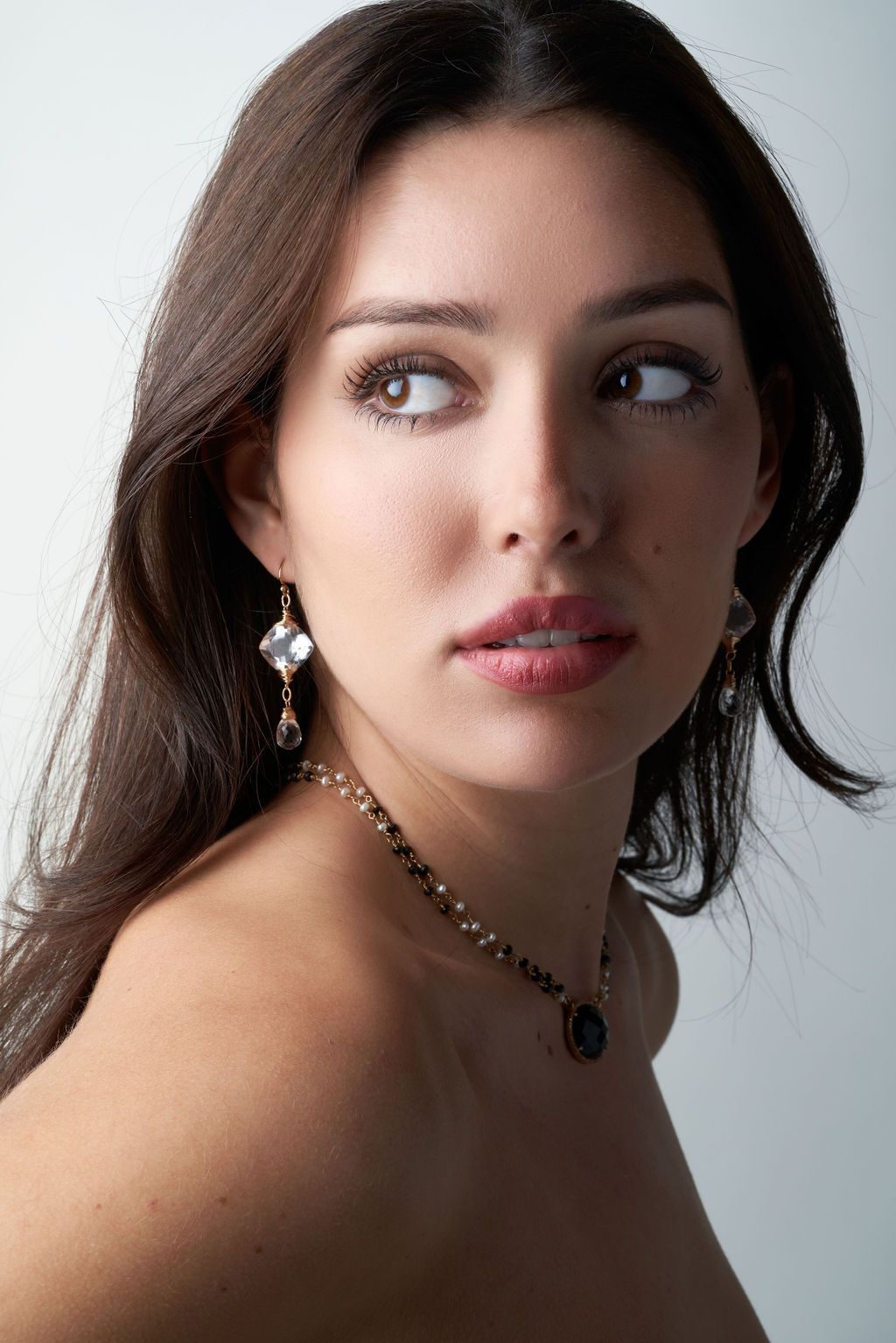 A woman wearing a necklace and earrings is looking at the camera.