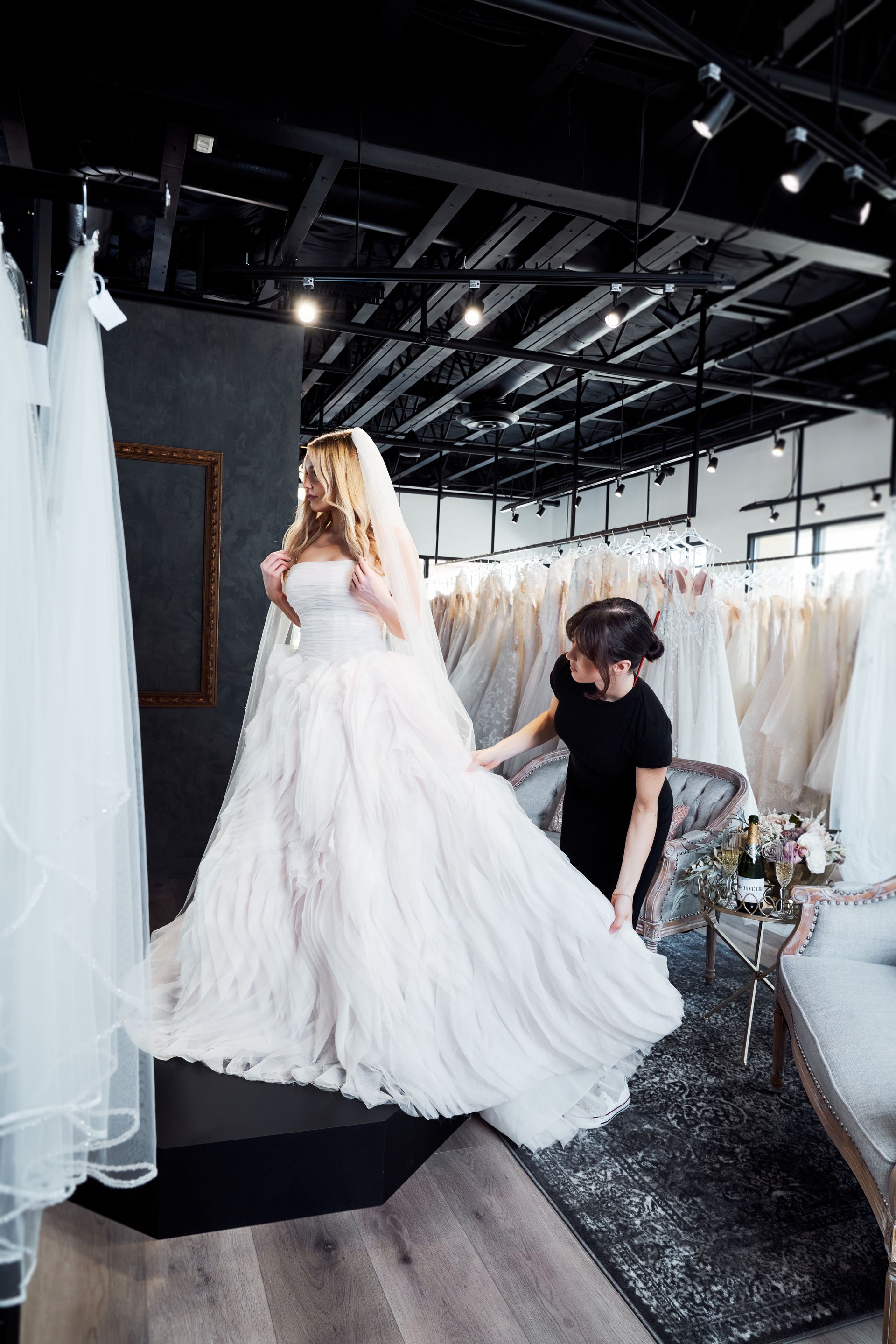 A woman is helping a woman try on a wedding dress in a bridal shop.