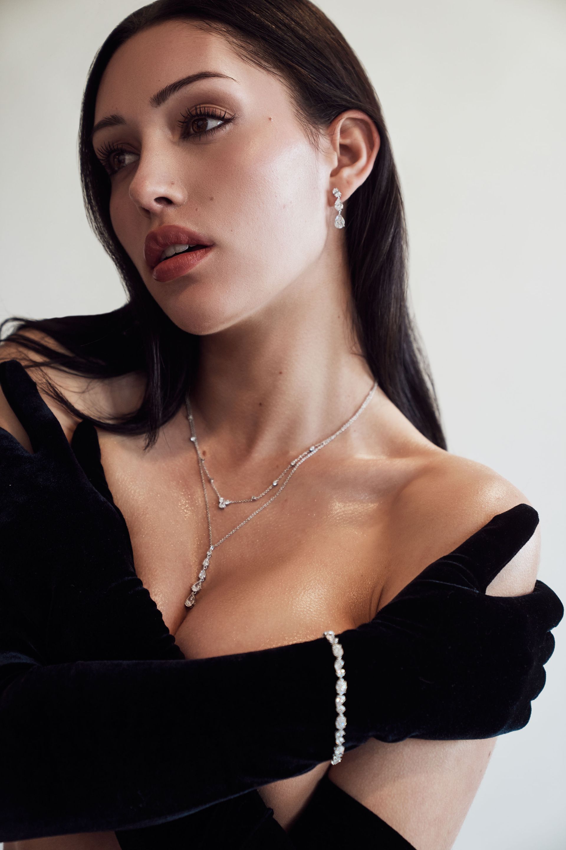 A woman in a black dress and gloves is wearing a necklace and bracelet.