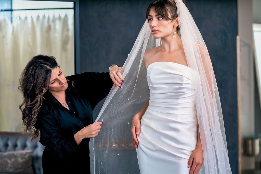 A woman is helping a woman in a wedding dress with her veil.