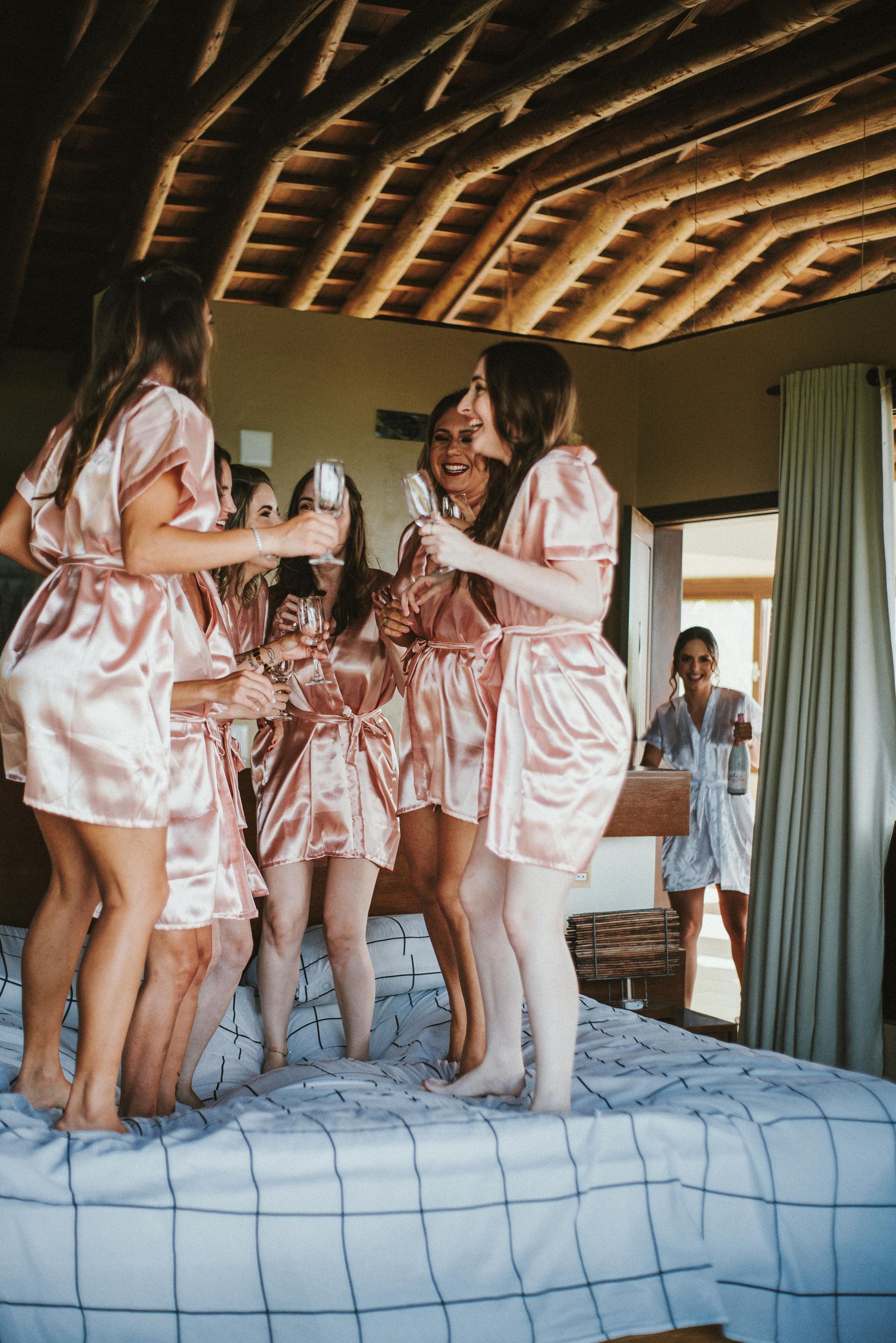 A group of women in pink robes are jumping on a bed.