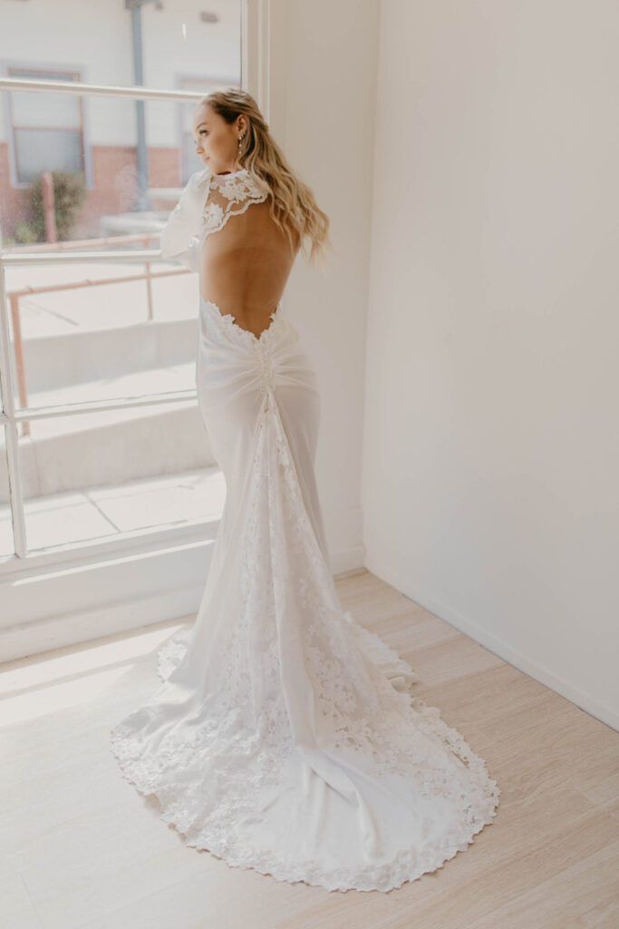 A woman in a white wedding dress is standing in front of a window.