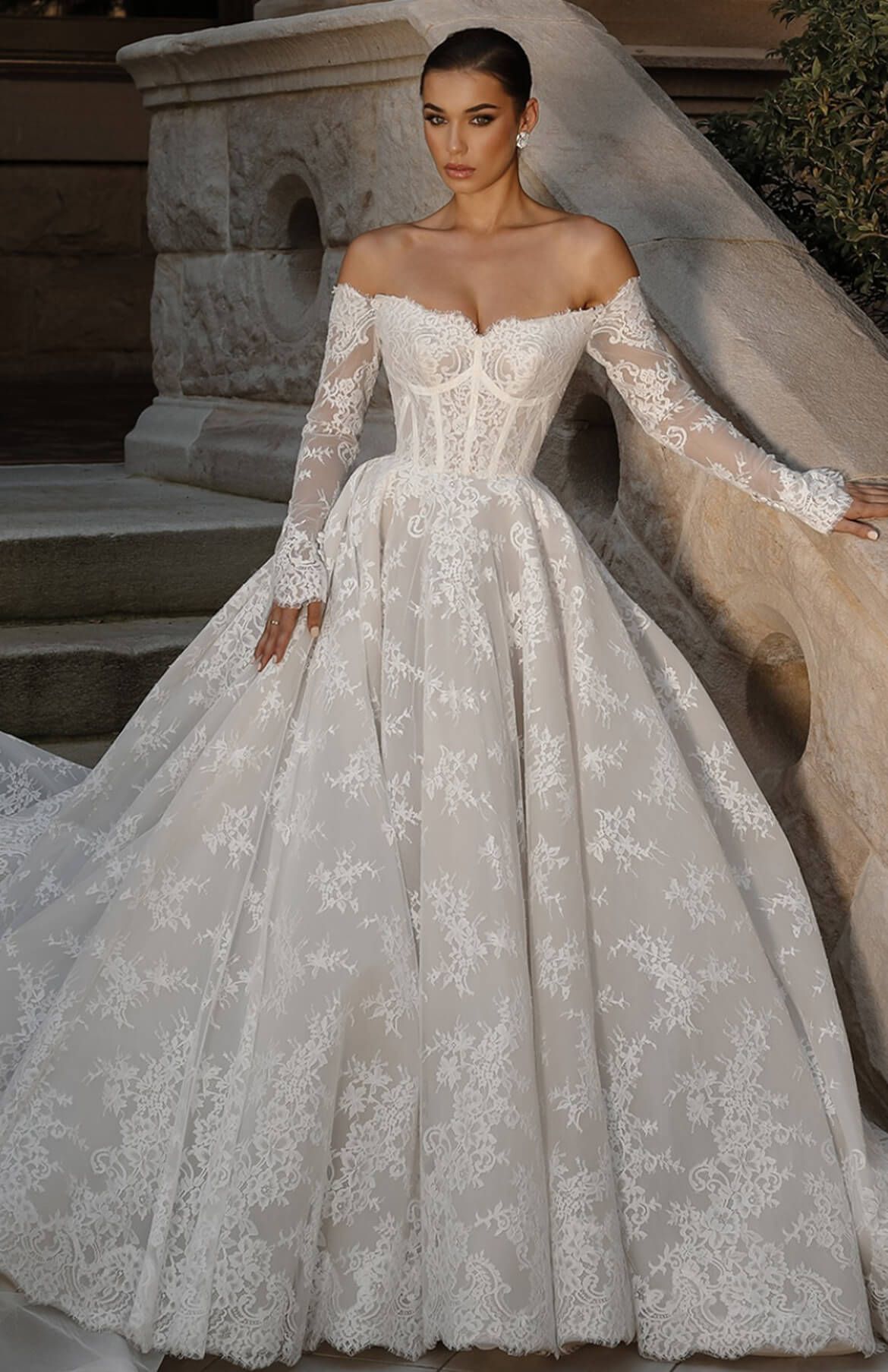 A woman is wearing a white lace wedding dress with long sleeves.