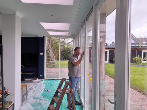 Iemand is bezig met glazen deuren met witte kozijnen in een lichte, moderne woonruimte 