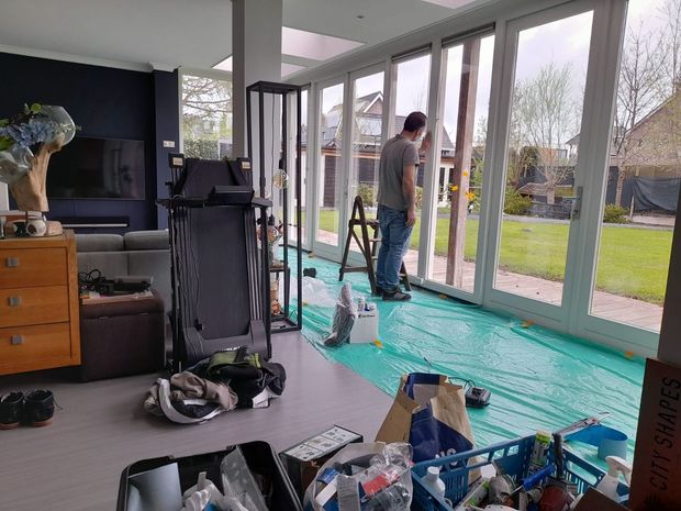 Iemand is bezig met schilderen van witte vouwdeuren van glas 