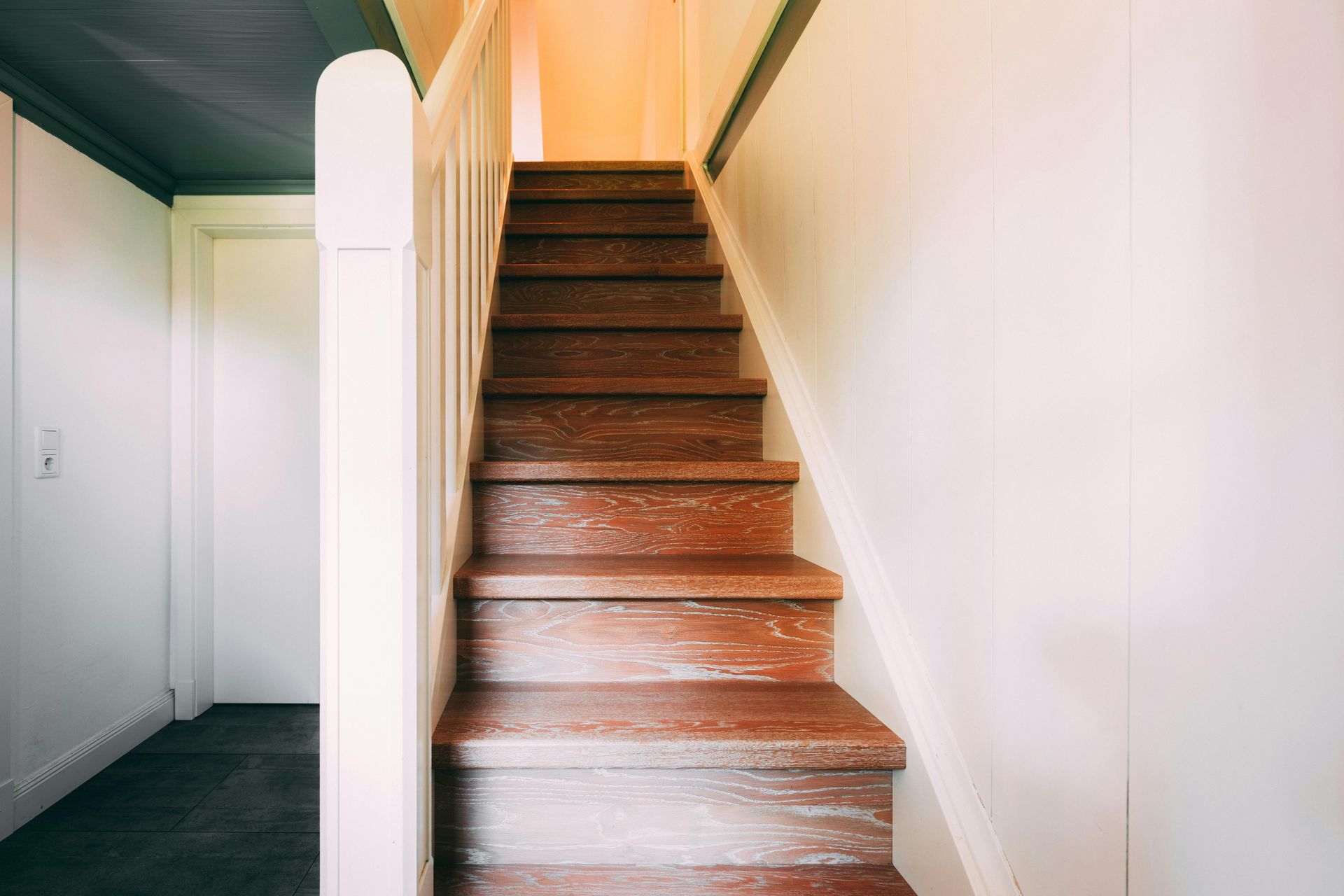 Een witte houten trap met bijpassende balustrade leidt naar een raam in een licht, modern interieur.