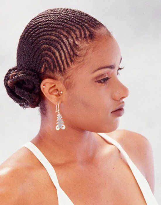 A woman with braided hair is wearing earrings and a white tank top