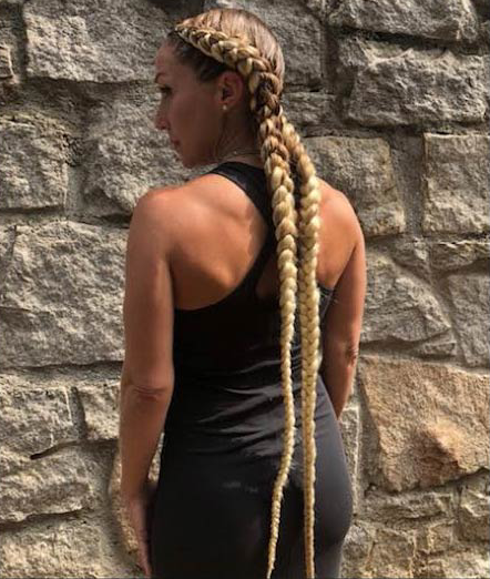 A woman with braids in her hair is standing in front of a brick wall.