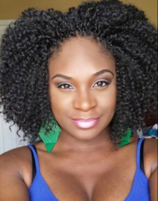 A woman with curly hair is wearing a blue tank top and green earrings