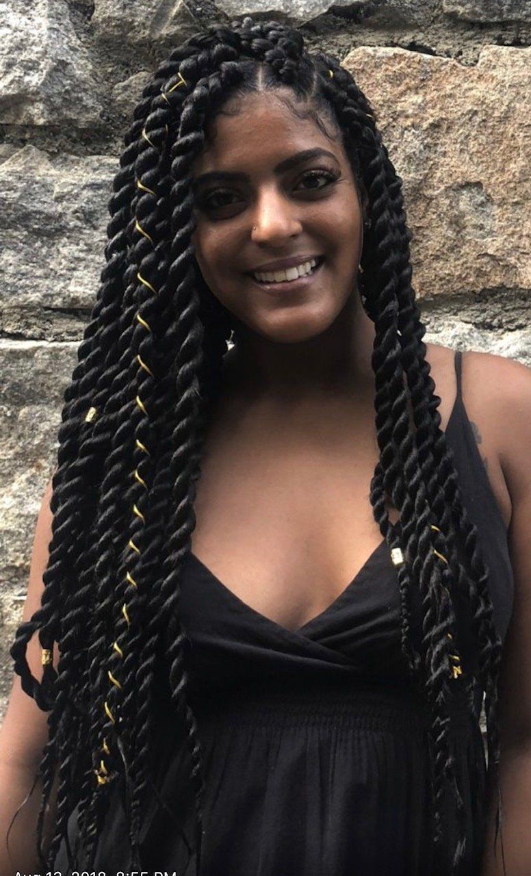 A woman with braids in her hair is wearing a black dress and smiling.