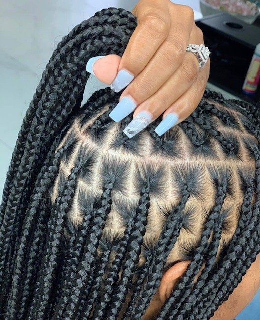 A woman with long blue nails and braids is holding her hair.