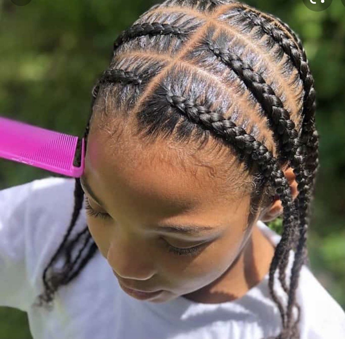 A young girl with braids is combing her hair with a pink comb.