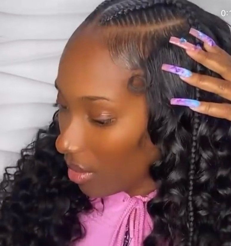 A woman with long nails and braids in her hair is wearing a pink shirt.