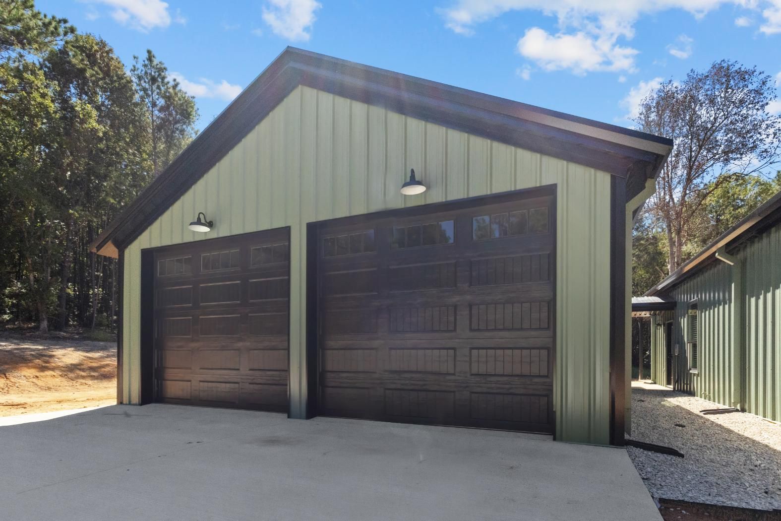Green metal garage with two dark brown doors and exterior lights, concrete drive.