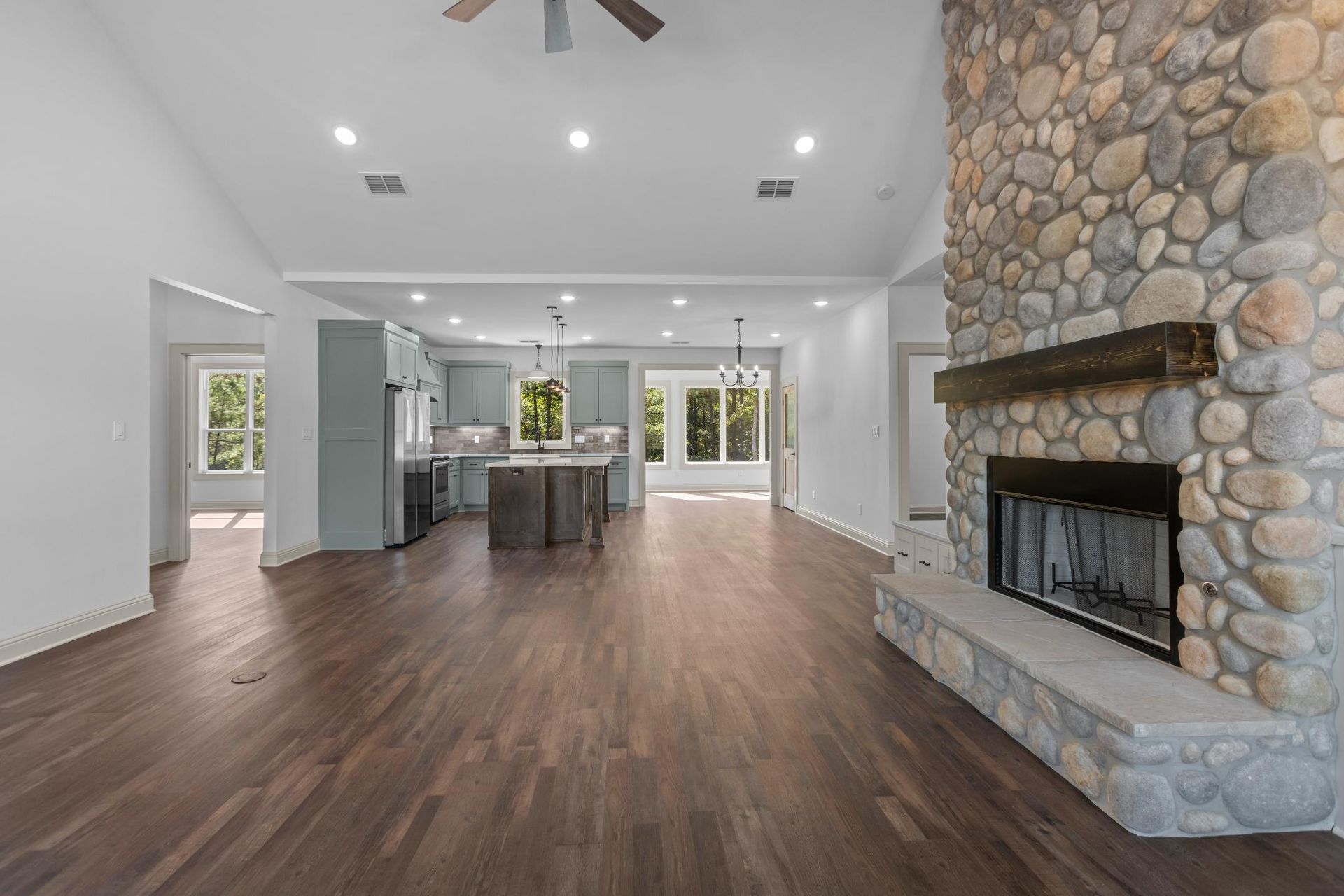 Open-concept living space with a stone fireplace, dark wood floors, and a gray kitchen.