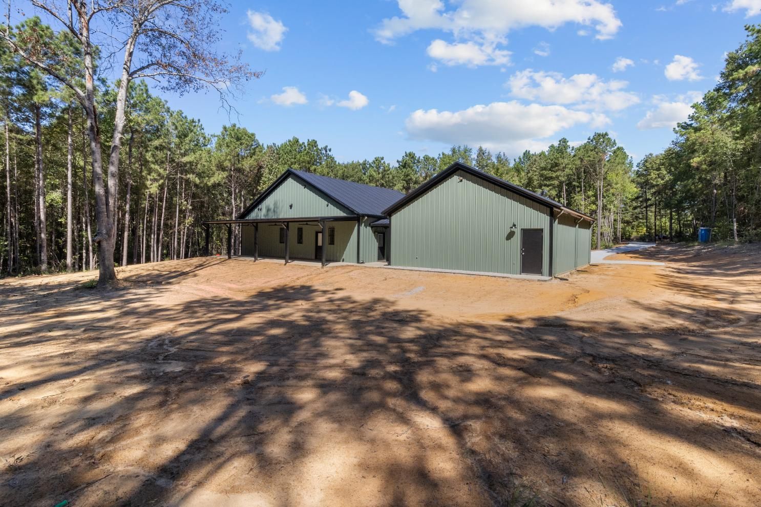 Green metal home in a wooded area, under a blue sky with clouds.