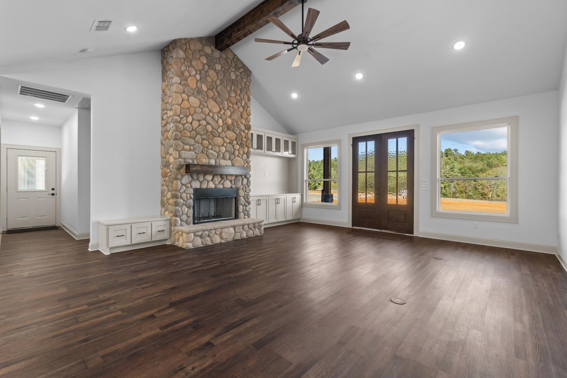 Living room with stone fireplace, hardwood floors, and double doors to outside.