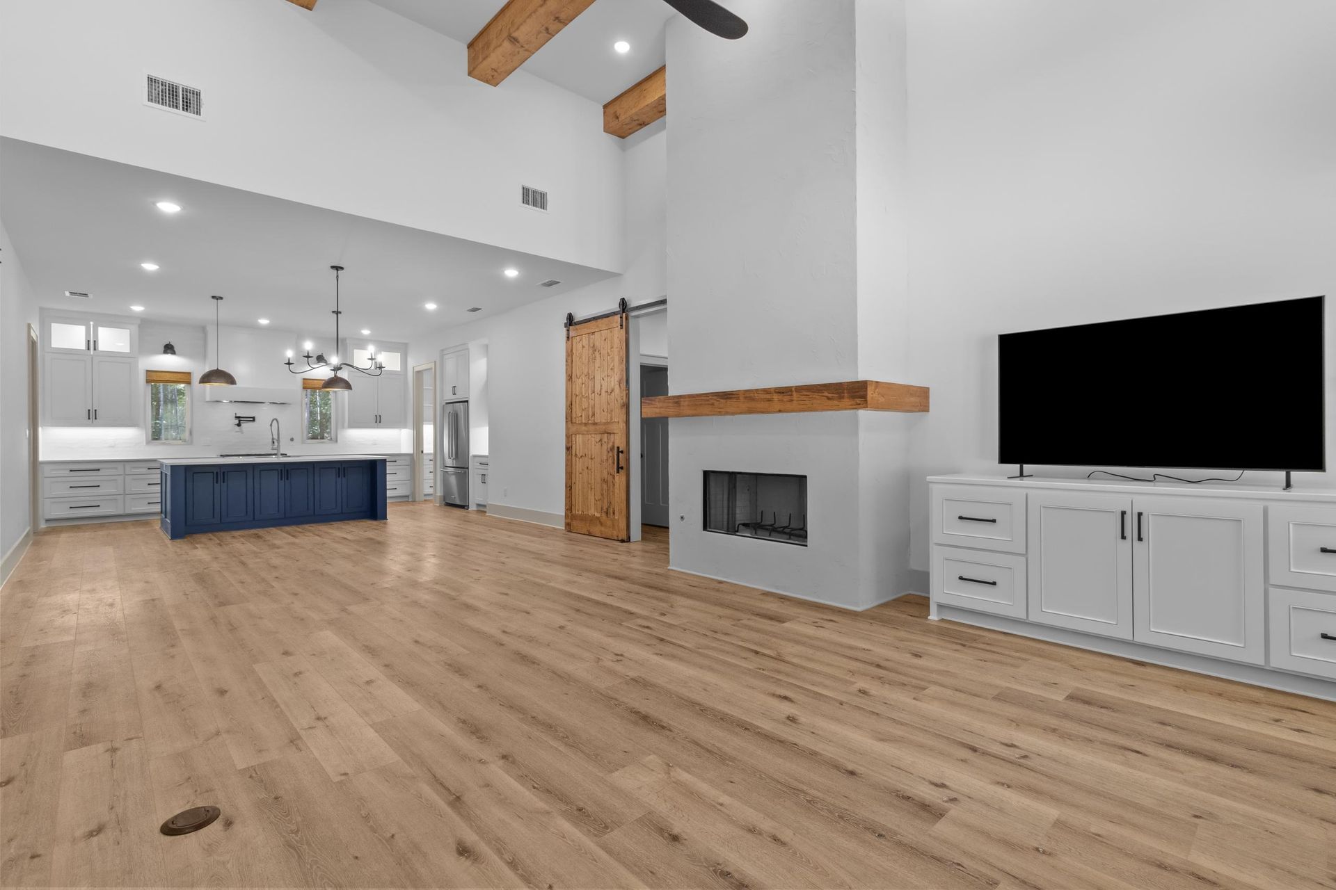 Modern living room with a kitchen. Light wood floors, white walls, fireplace, and a TV.