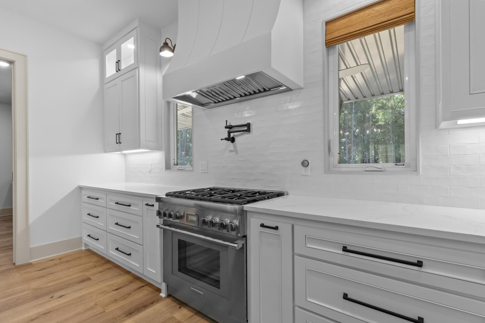 Modern white kitchen with stainless steel range, white cabinets, and light wood floors.