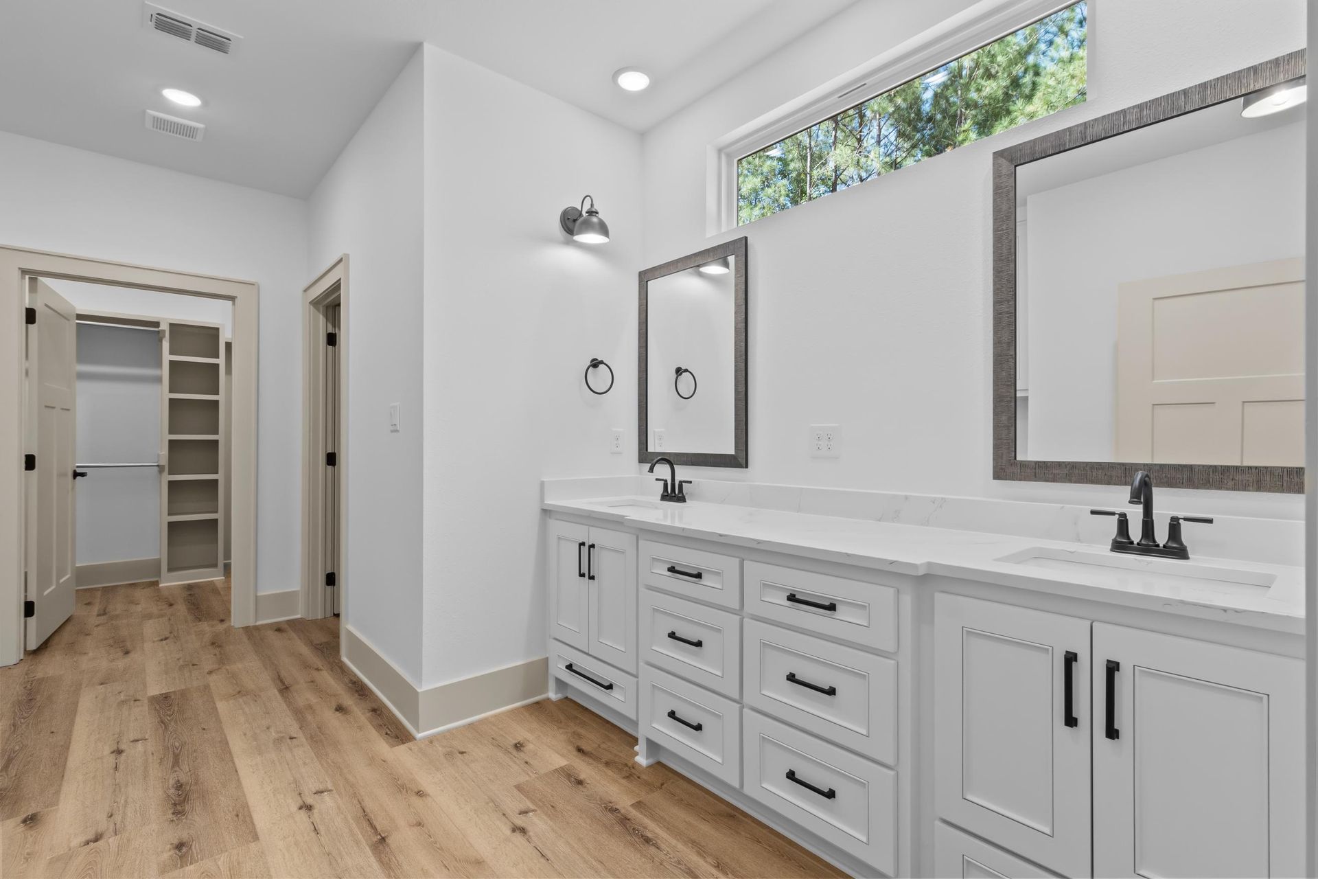 Spacious white bathroom with double vanity, black fixtures, large mirrors, and a walk-in closet.