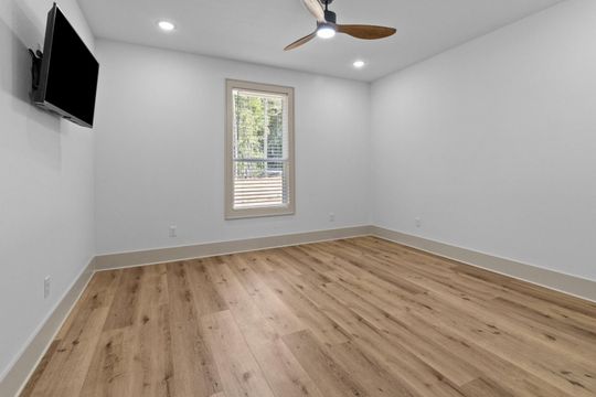 Empty room with wood floors, white walls, a window, ceiling fan, and a mounted TV.