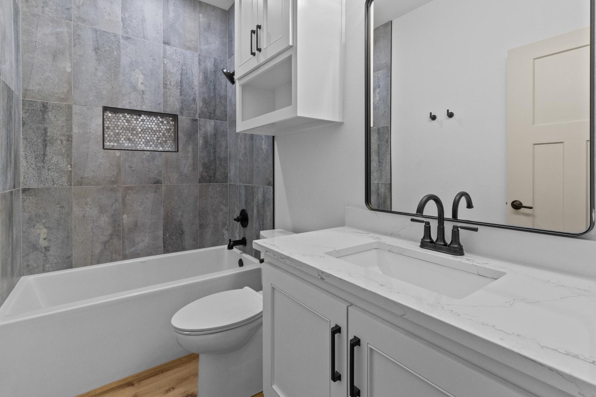 Modern bathroom with gray tiled walls, white vanity, and bathtub.