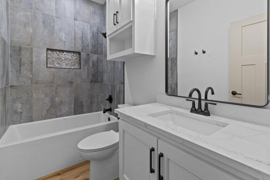 Modern bathroom with gray tiled walls, white vanity, and bathtub.