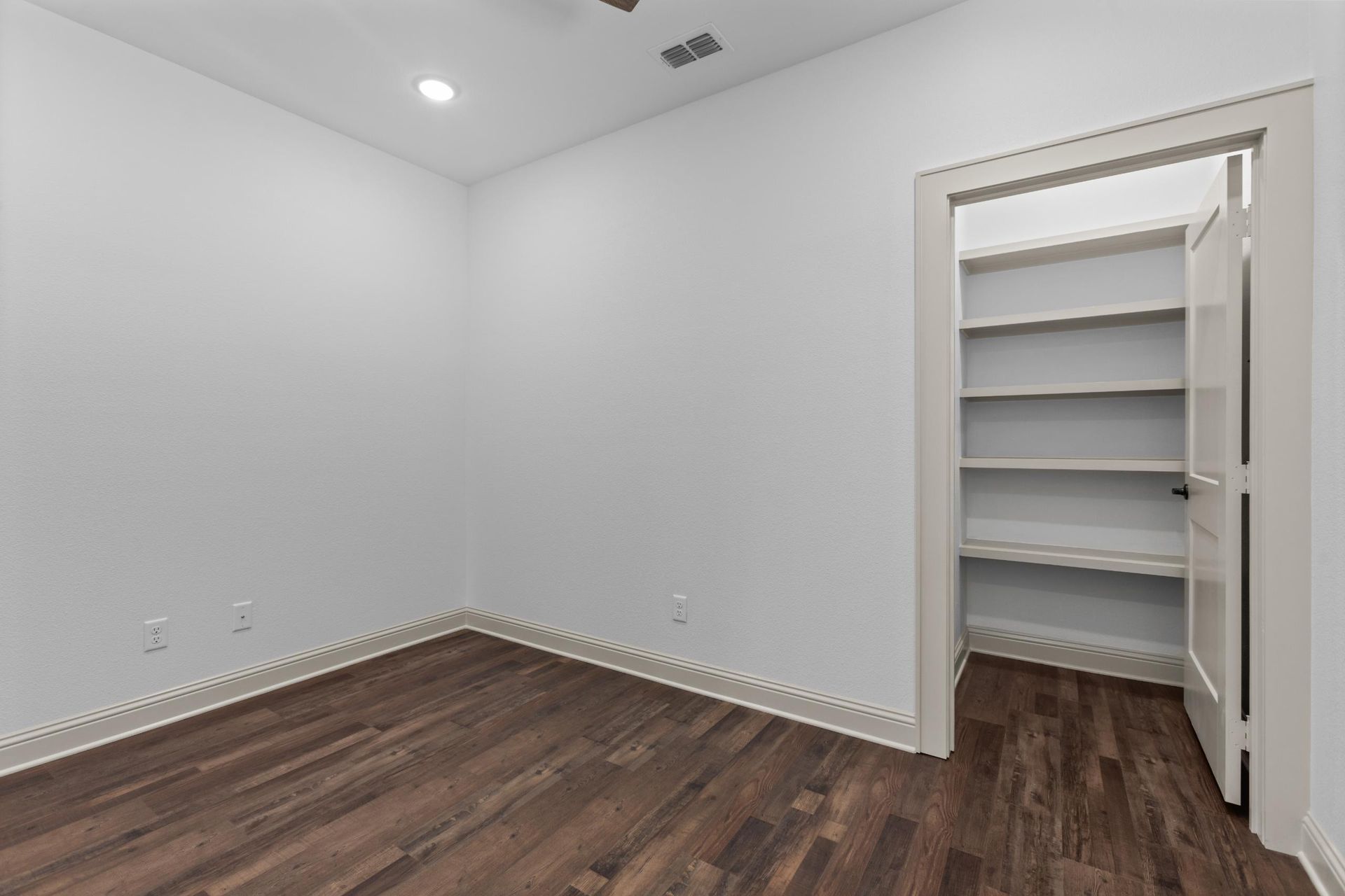 Empty room with dark wood floor and walk-in closet with shelves. White walls and trim.
