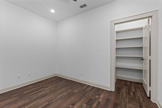Empty room with dark wood floor and walk-in closet with shelves. White walls and trim.