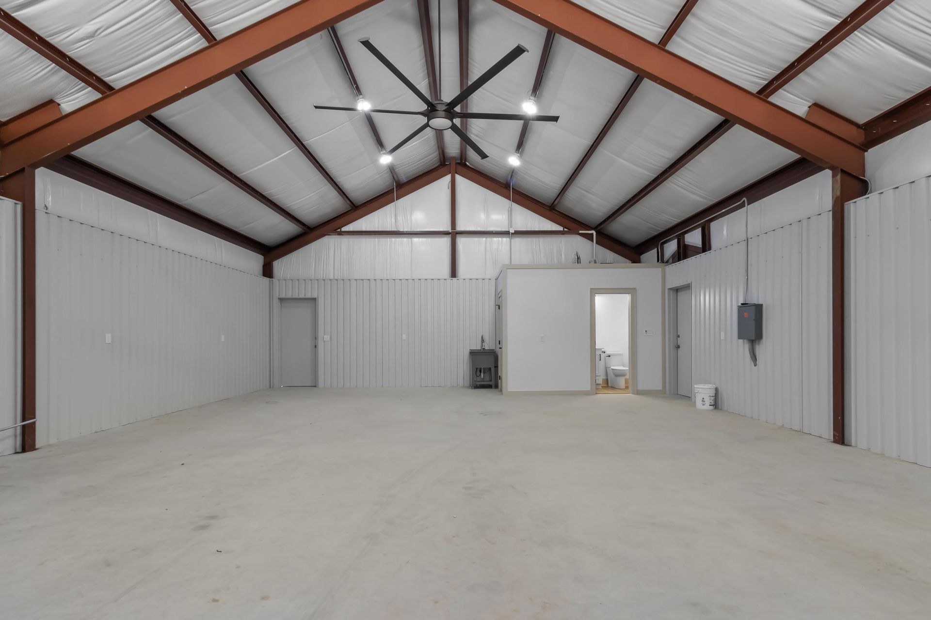 Empty metal warehouse interior with high ceilings, large fan, and concrete floor.