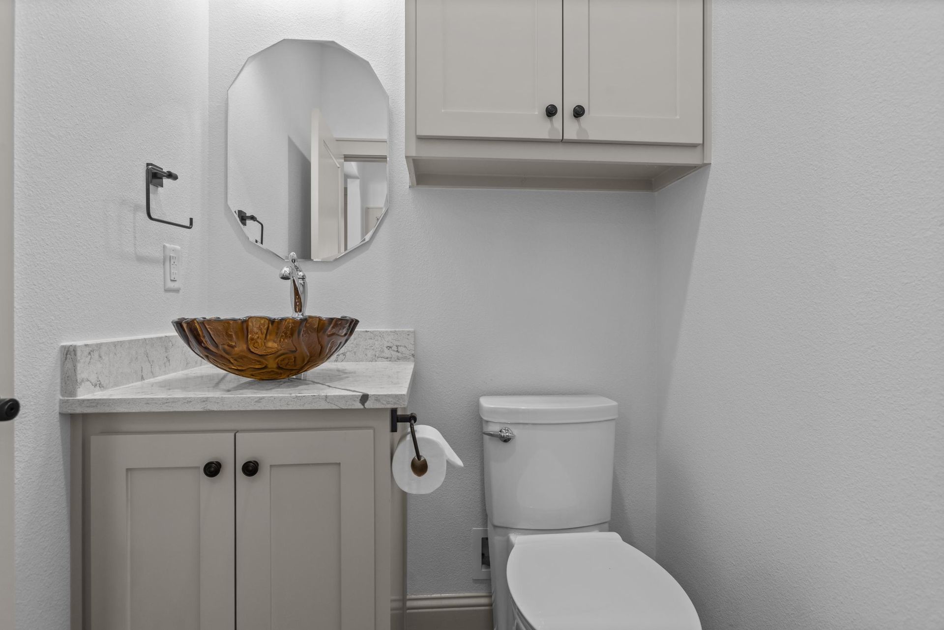 Small bathroom with a tan vanity, sink, mirror, toilet, and wall-mounted cabinet.