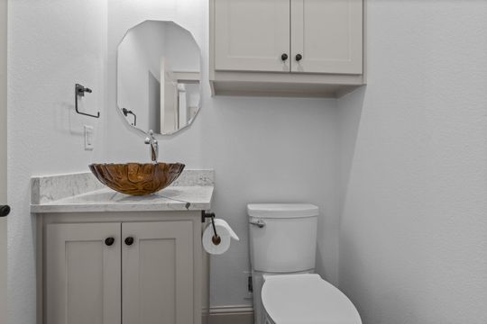 Small bathroom with a tan vanity, sink, mirror, toilet, and wall-mounted cabinet.