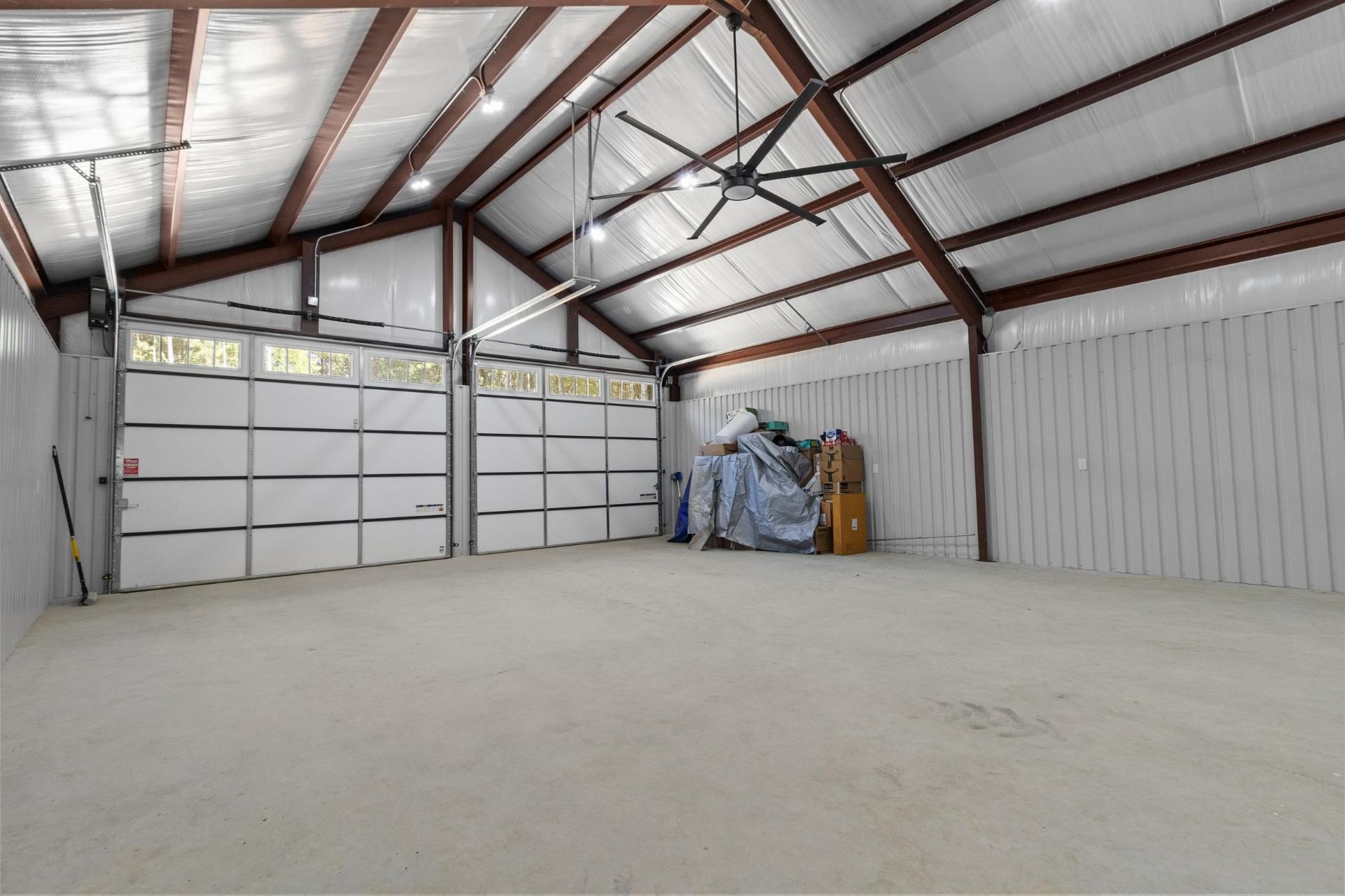 Empty metal building interior with white doors, concrete floor, and brown beams.