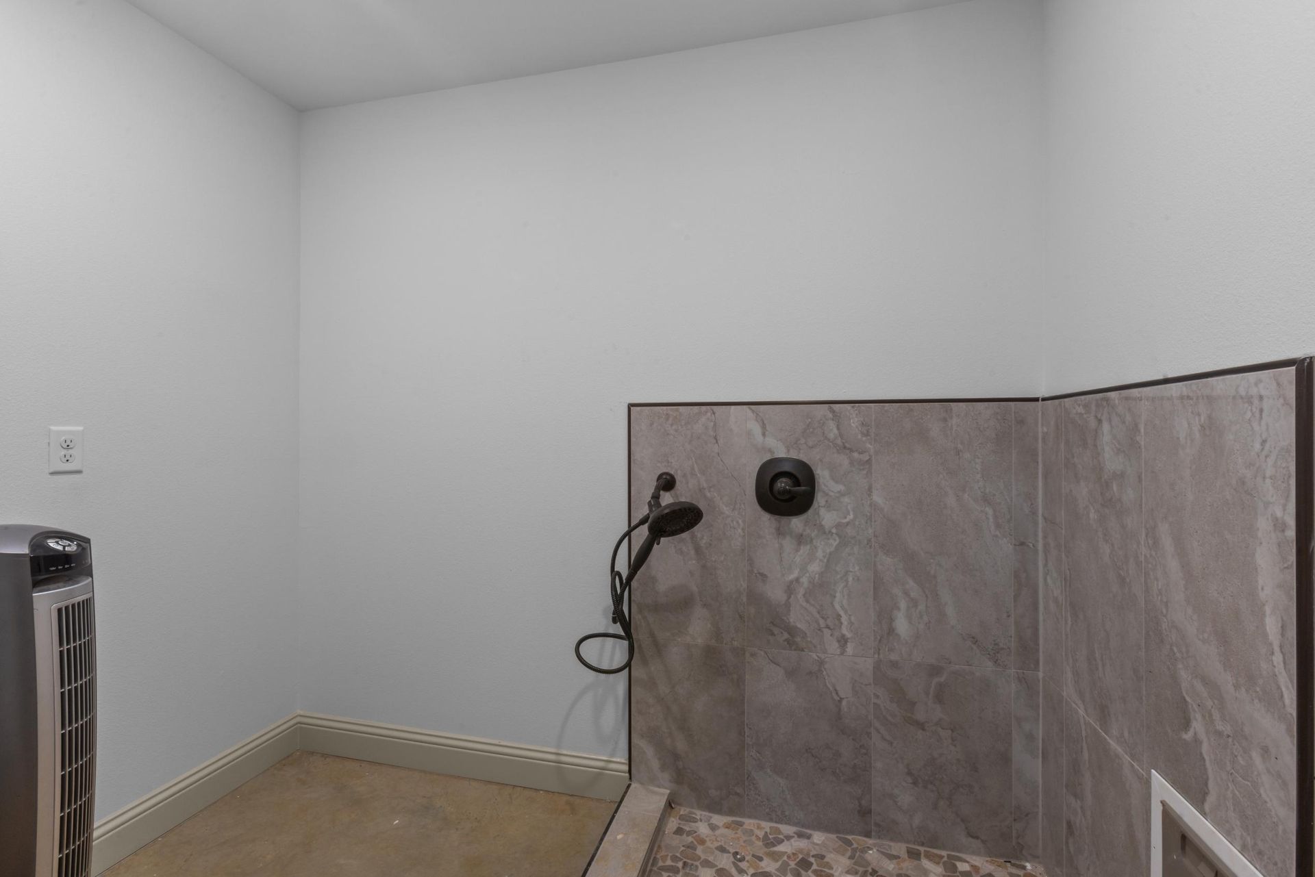 A dog shower with gray tile walls and shower head, set in a small room.