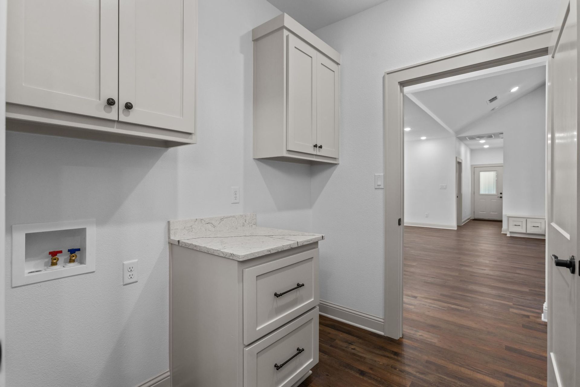 Laundry room with white cabinets, countertop, and washer connections. Doorway leads to hardwood floor.