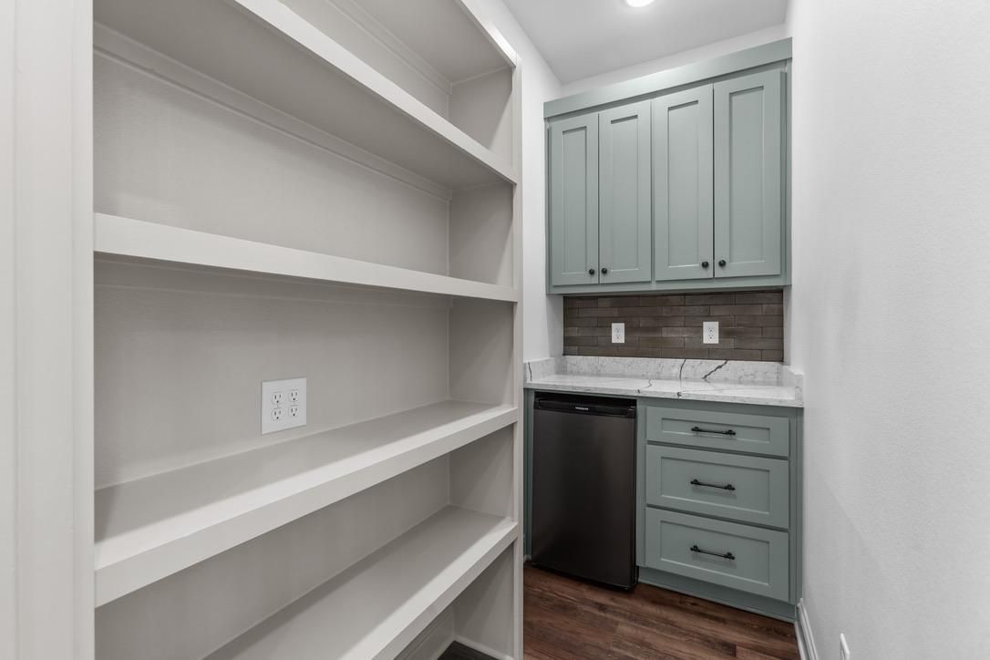 Pantry with built-in shelves and cabinets. Features gray-blue cabinets, stainless steel appliance, and wooden floors.